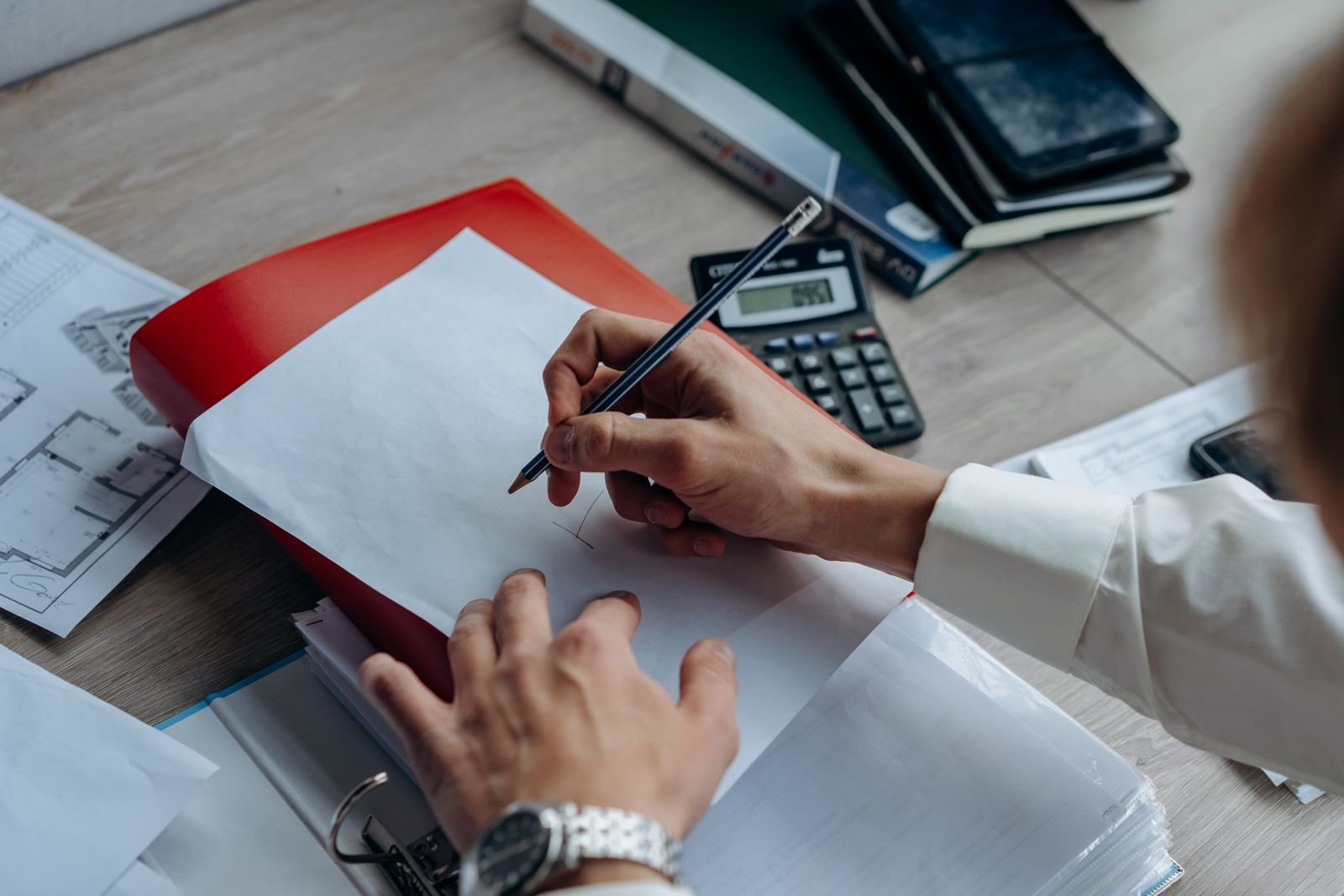 Mãos escrevendo em papel com calculadora e caderno, calculando custos da viagem