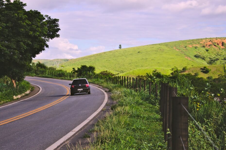 Carro trafegando em uma estrada rural sinuosa no interior do Brasil, cercada por vegetação