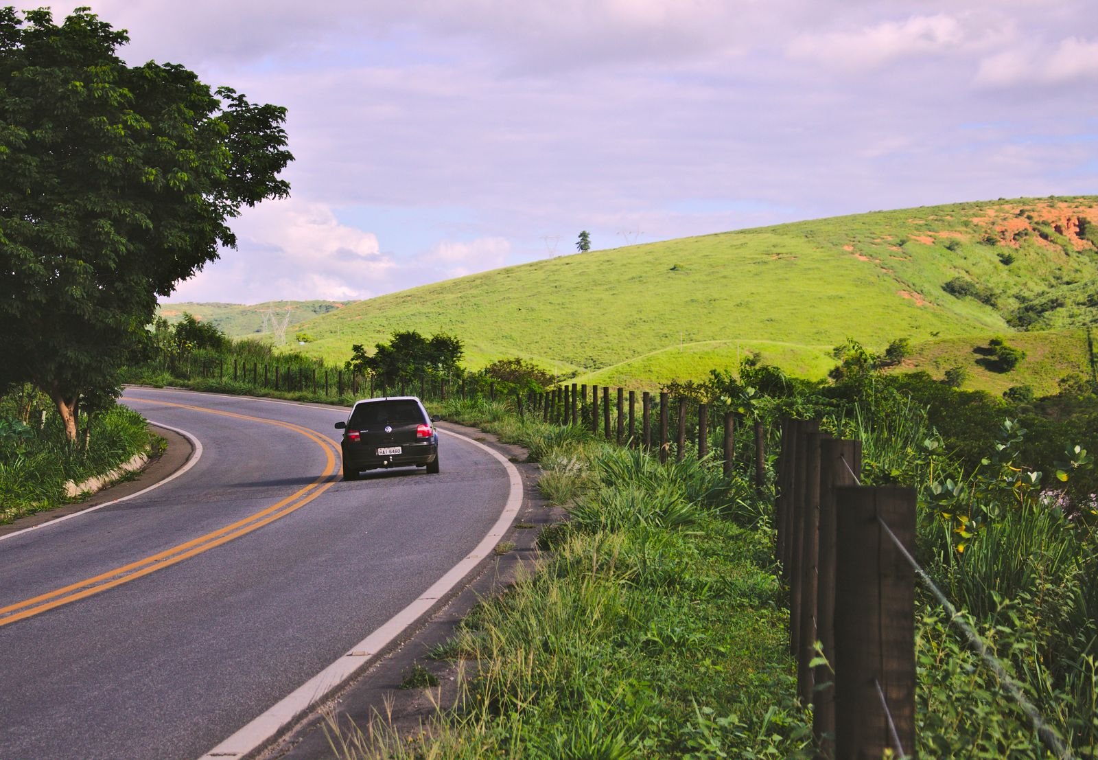 Carro trafegando em uma estrada rural sinuosa no interior do Brasil, cercada por vegetação