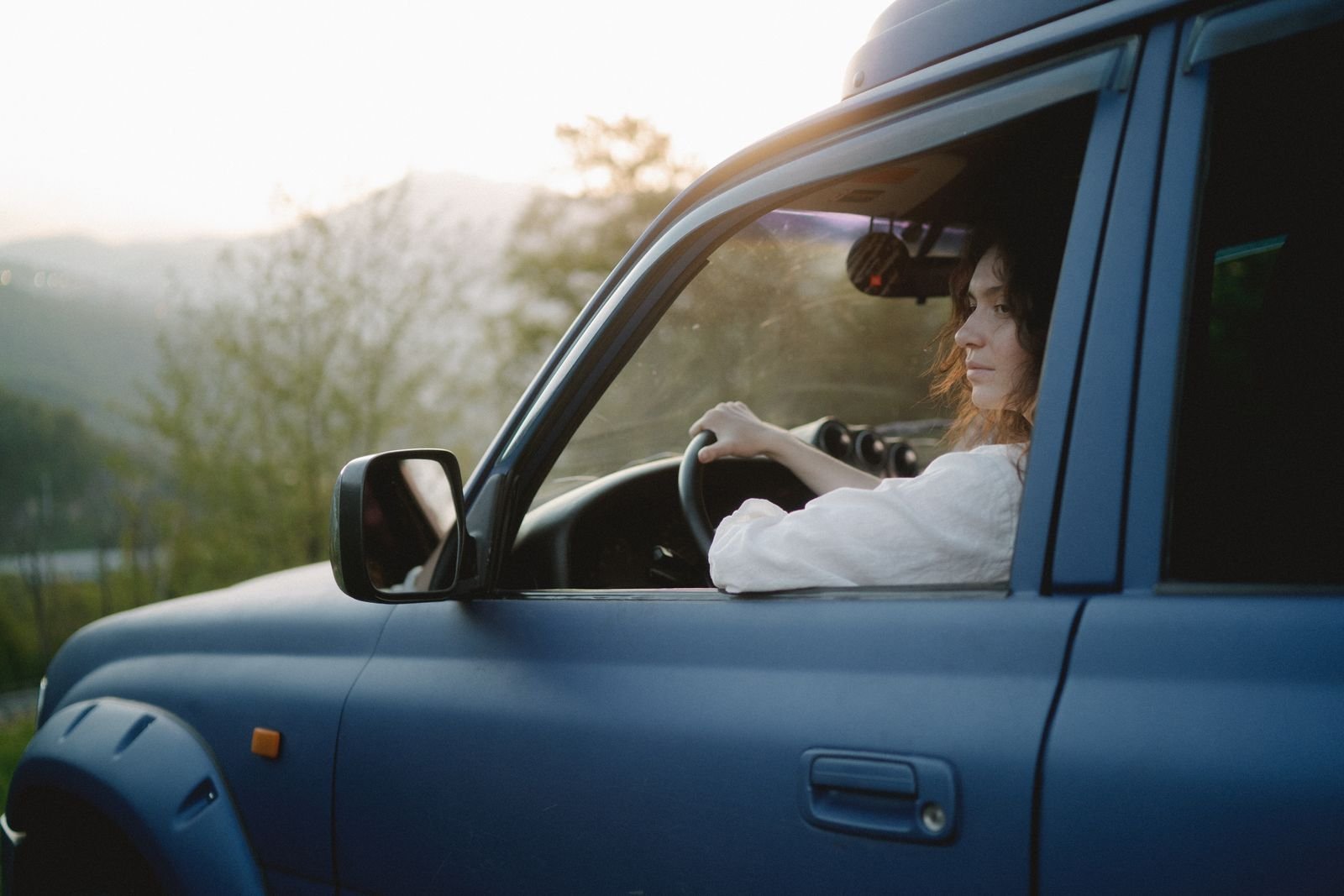 Mulher dirigindo um SUV por uma paisagem cenica ao por do sol, explorando sozinha