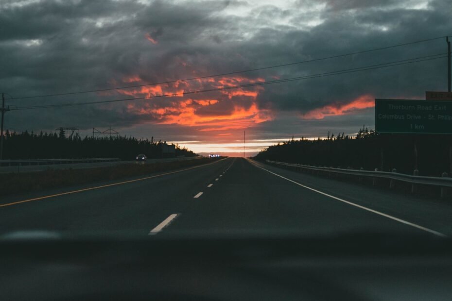 Vista do painel do carro dirigindo em direcao a um por do sol dramatico na rodovia