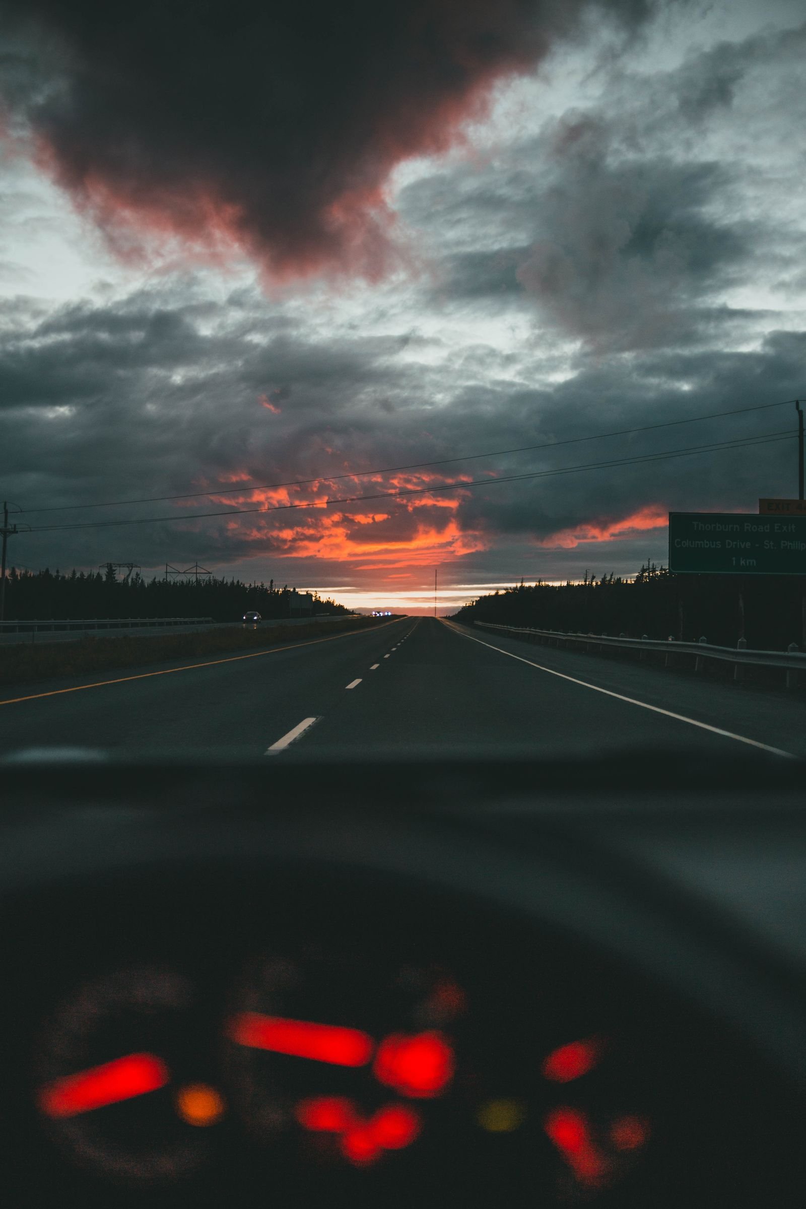 Vista do painel do carro dirigindo em direcao a um por do sol dramatico na rodovia